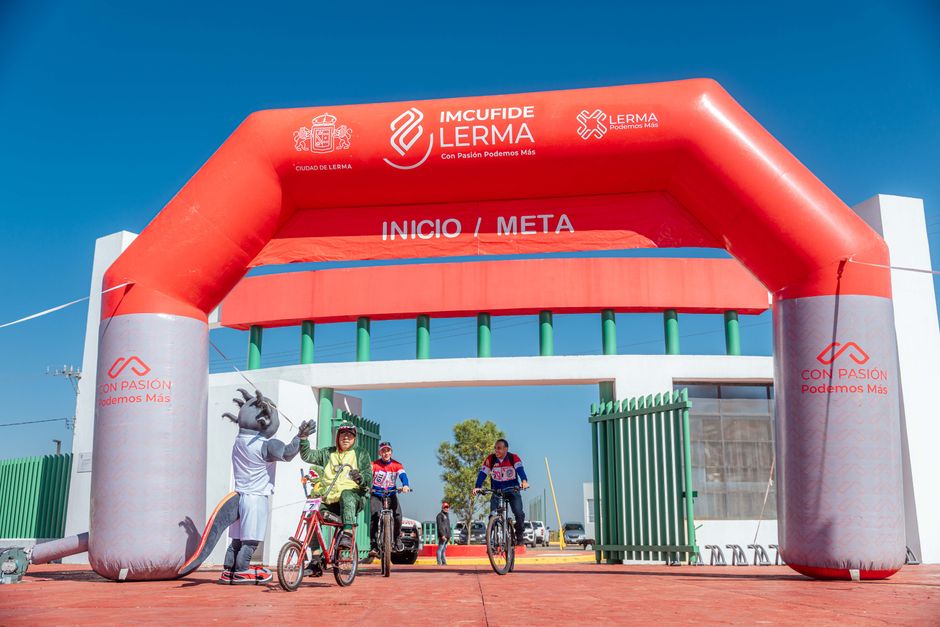 Un groupe de cyclistes sur la ligne de départ à Lerma sous un arc gonflable rouge avec une mascotte.
