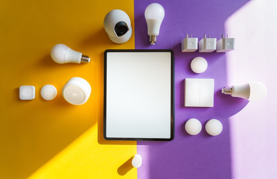 Vue de dessus des appareils de maison intelligente et d'une tablette sur un fond jaune et violet divisé.