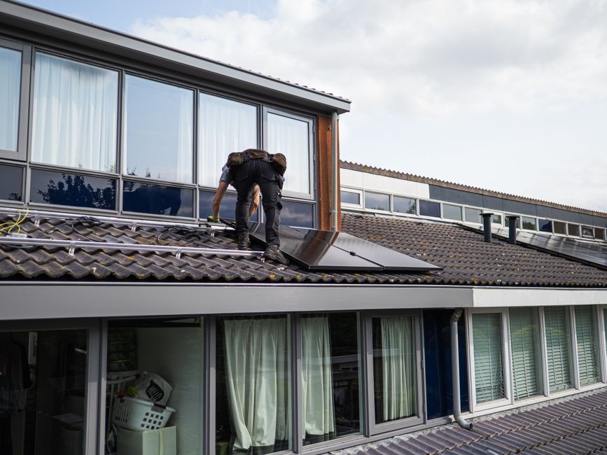 Technicien travaillant à l'installation de panneaux solaires sur un toit résidentiel pendant la journée.