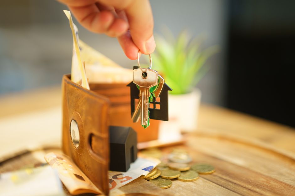 Gros plan d'une main tenant une clé de maison avec un portefeuille et des pièces de monnaie, symbolisant un investissement immobilier.