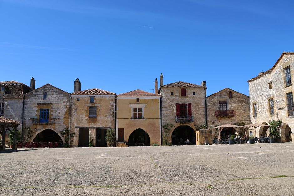 De beaux bâtiments en pierre sur une place de village pittoresque sous un ciel bleu clair.