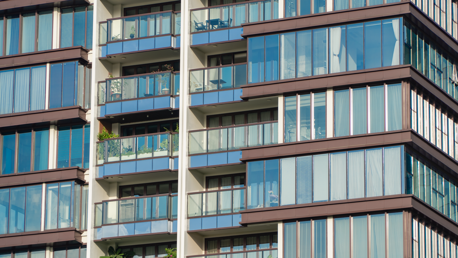 Vue en gros plan de la façade moderne en verre d'appartements avec balcons et reflets.
