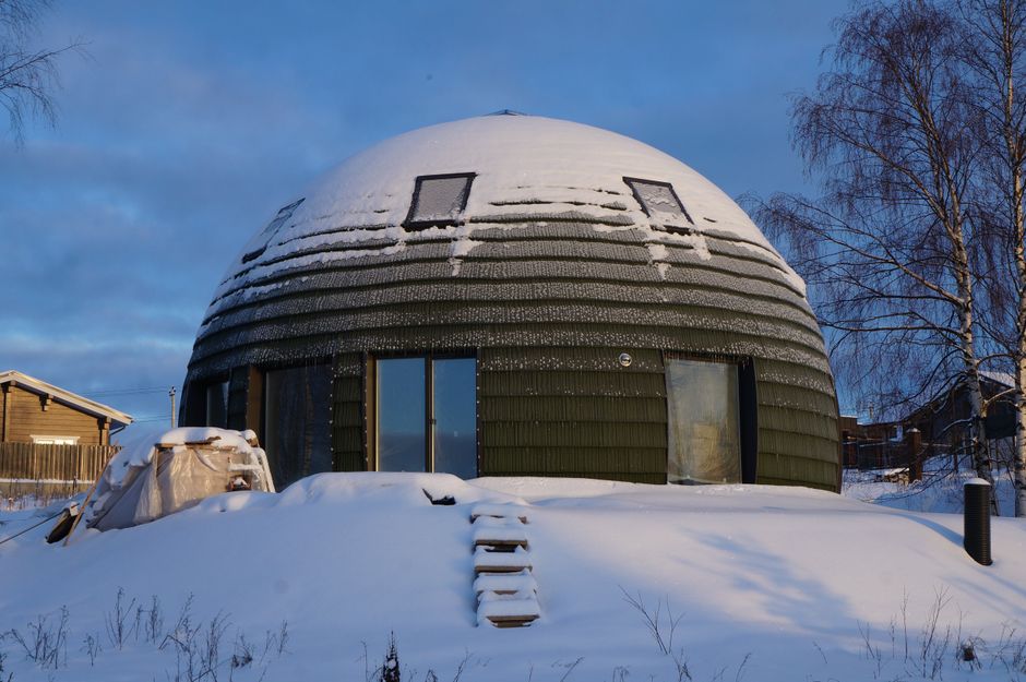 Une maison en forme de dôme unique recouverte de neige en hiver, créant un paysage serein.