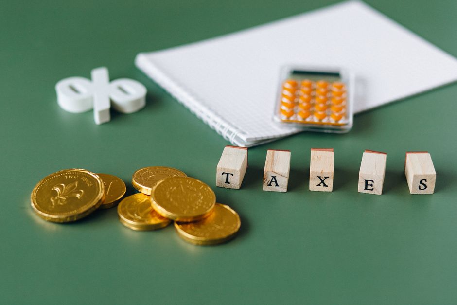 Gros plan sur des objets liés aux impôts comprenant des pièces de monnaie, une calculatrice et le mot 'impôts' sur un fond vert.