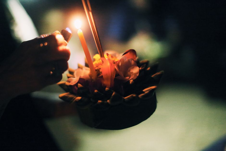 Photo nocturne atmosphérique d'une main lâchant un krathong avec des bougies, célébrant le festival de Loy Krathong.