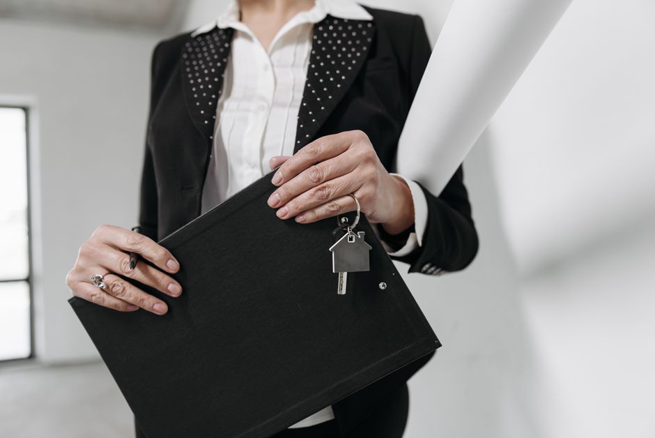 Gros plan d'un agent immobilier tenant un porte-clés et un carnet avec un fond de bureau intérieur.