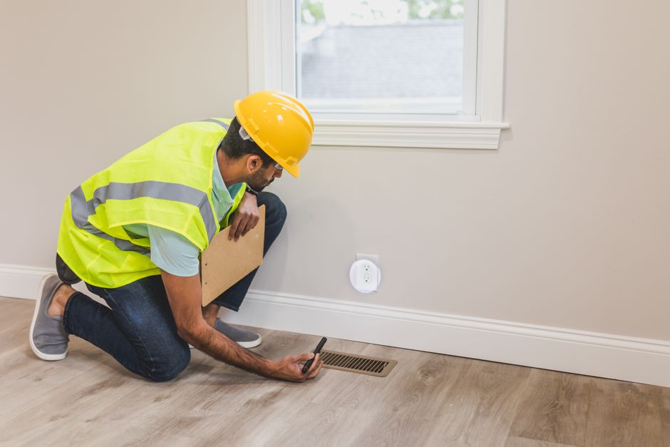 Un ouvrier du bâtiment en casque inspecte une grille de sol à l'intérieur, garantissant les normes de qualité et de sécurité.