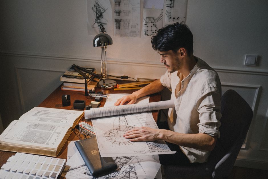 Jeune architecte à un bureau travaillant sur des plans sous la lumière d'une lampe.